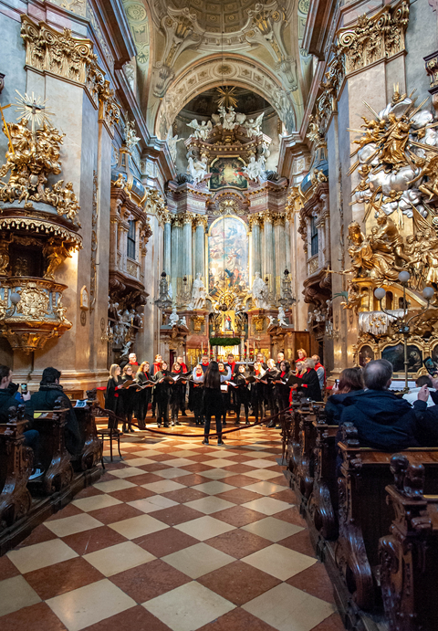 Śpiewamy nasz koncert tuż przed ołtarzem. Ujęcie jest z daleka, nieomal z wejścia do świątyni więc widać nas na tle bogatego wystroju, pełnego złota i dramatycznie upozowanych barokowych figur.